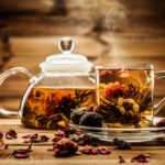 Teapot and glass cup with blooming tea flower inside against wooden background